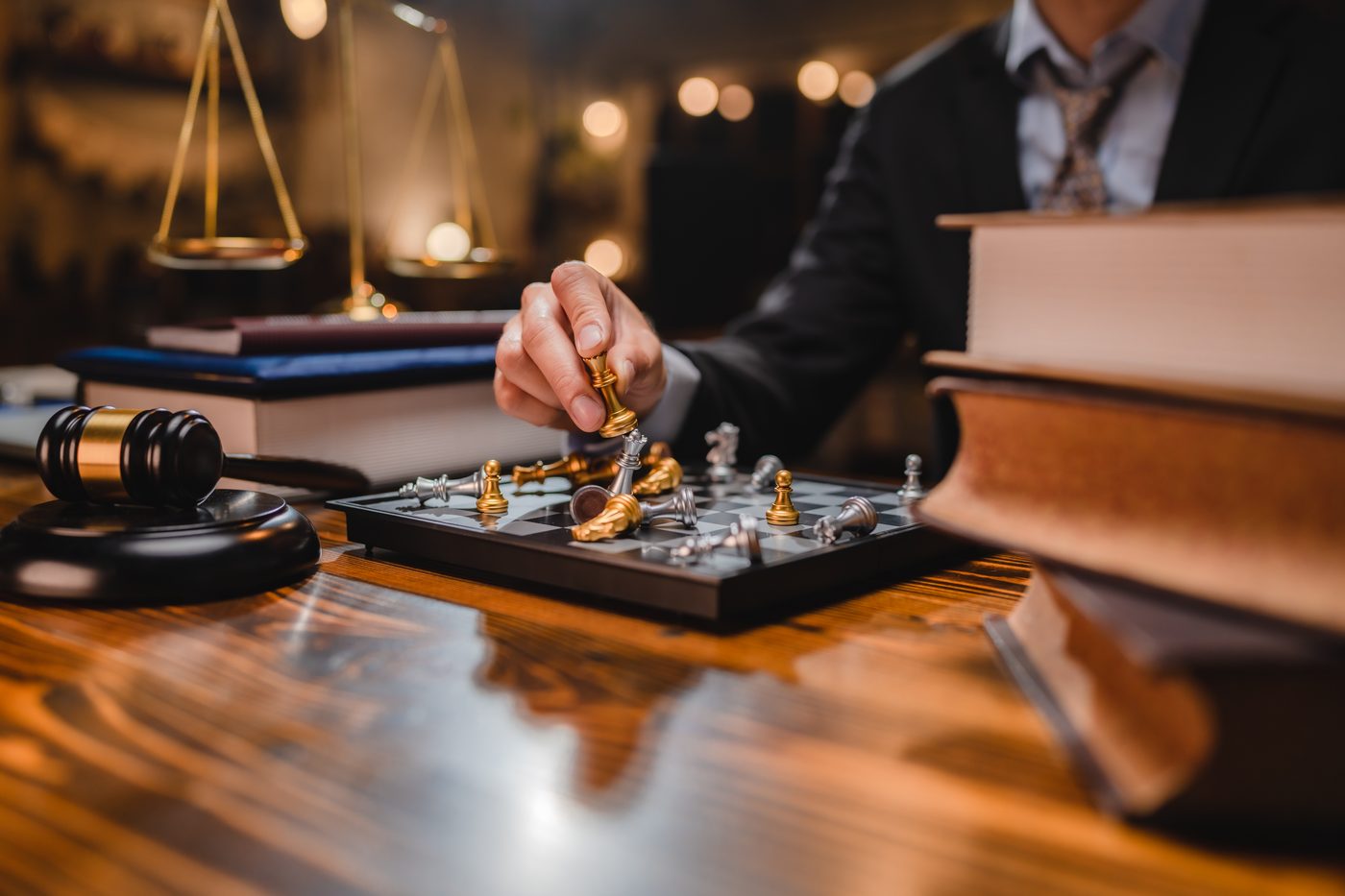 A hand moving a piece on a chessboard beside the scales of justice — building a New York defense strategy