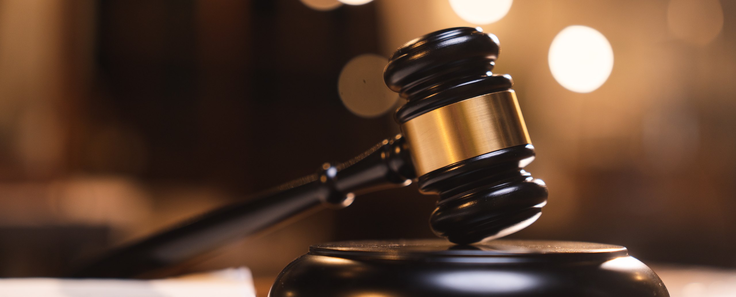 A judge’s gavel resting on its block, warm courtroom lights blurred behind